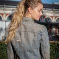 How to style long hair: Outdoor profile shot of a blonde model with long wavy hair in a high double ponytail, wearing a denim jacket
