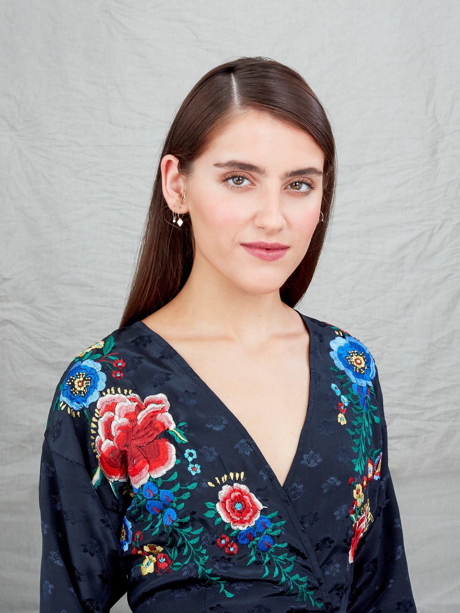 How to style long hair: Studio image of a brunette model with long straight hair styled in a sleek side parting, wearing a floral top