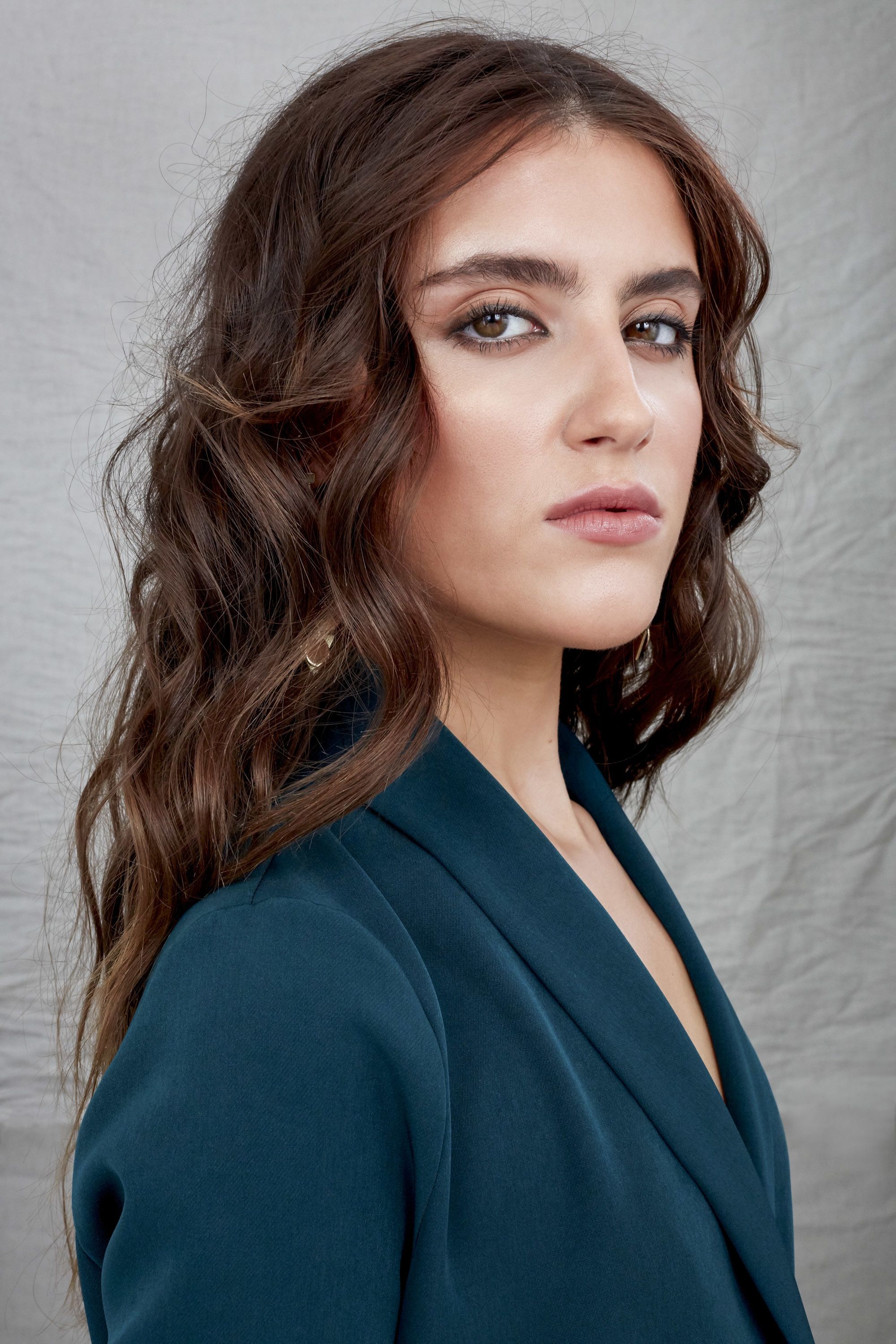 How to style long hair: Studio photo of a brunette woman with voluminous Victoria's Secret waves, wearing a teal blazer dress