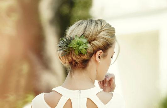 back view of a blonde model wearing a white cut out dress with her hair in a gibson tuck with succulents clipped into it