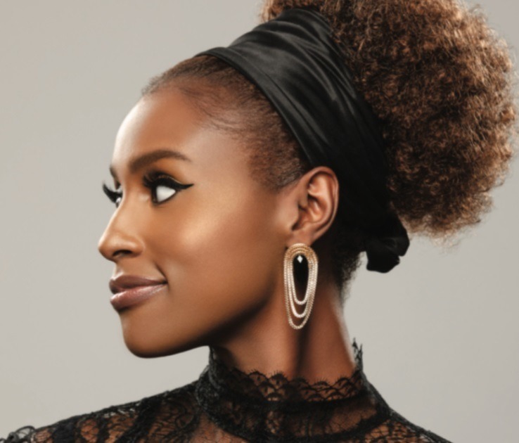 close up shot of issa rae with a curly ponytail with a headband silk scarf on, wearing earrings and posing
