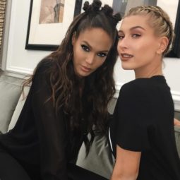 Joan Smalls with bantu knots hairstyle in a half-up look, sat next to a blonde model with a halo braid