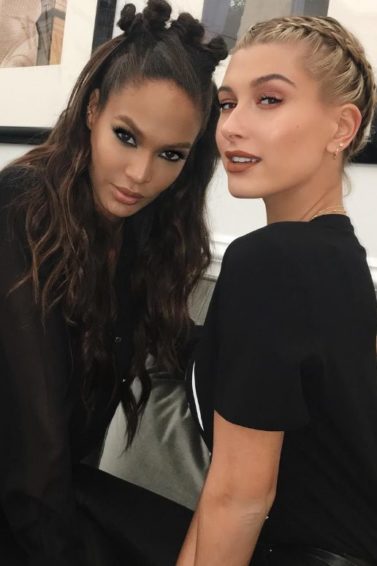 Joan Smalls with bantu knots hairstyle in a half-up look, sat next to a blonde model with a halo braid