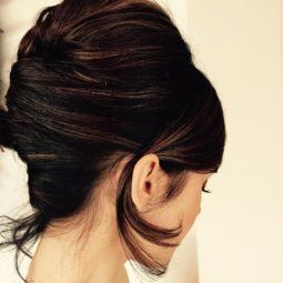back view of actress Lily Collins with her dark brown hair worn in a french twist updo and one piece of hair tucked behind her ear
