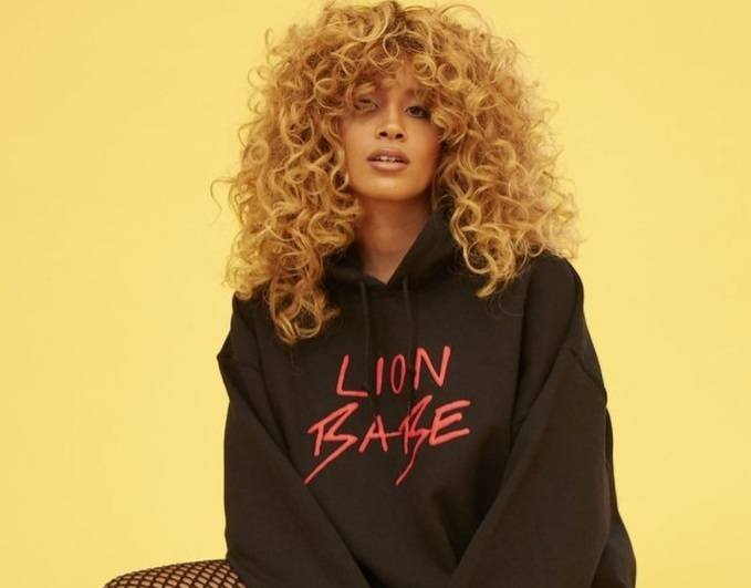 close up shot of lion babe with big blonde curly hair, wearing jumper in a studio