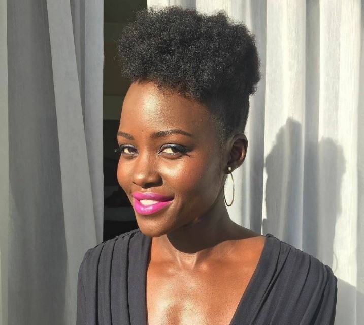 lupita nyong'o with an afro pompadour wearing a black outfit and pink lipstick