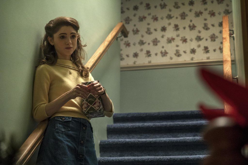 nancy from stranger things with her brunette hair pinned back into a half up look wearing a yellow top and blue jeans