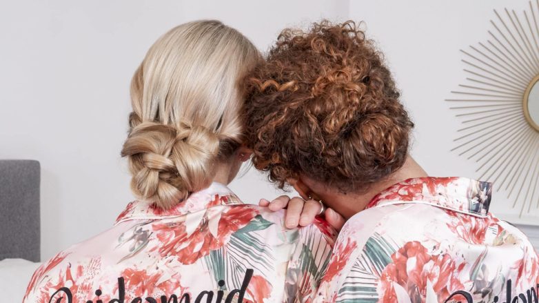 wedding chignon: back view of two bridesmaids, one with blonde straight hair and the other with curly golden brown hair both with their hair in low chignon wedding hairstyles