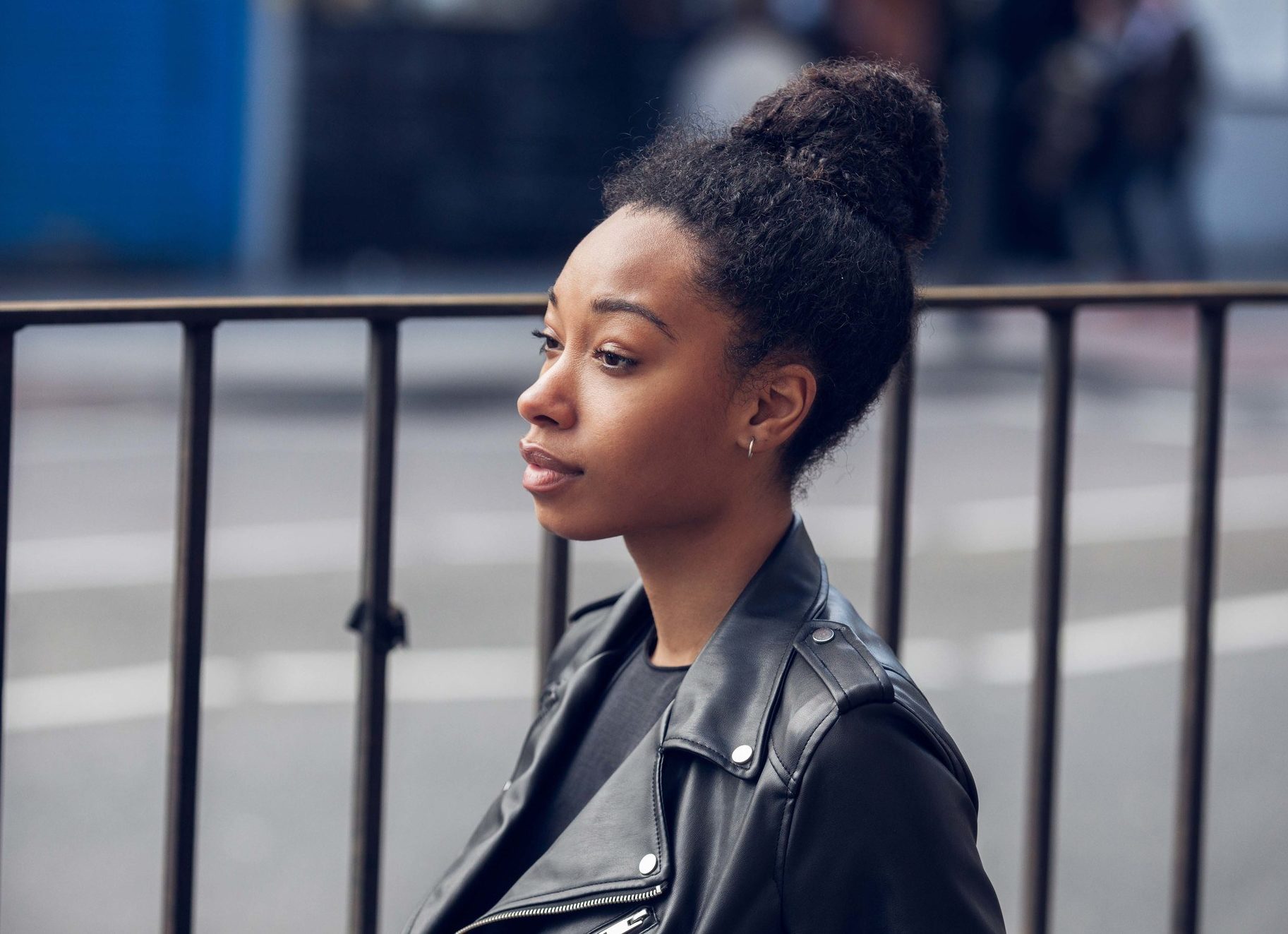Curly hair hairstyles: Side profile of a black woman with natural hair styled in a high bun in street style picture wearing a black leather jacket.