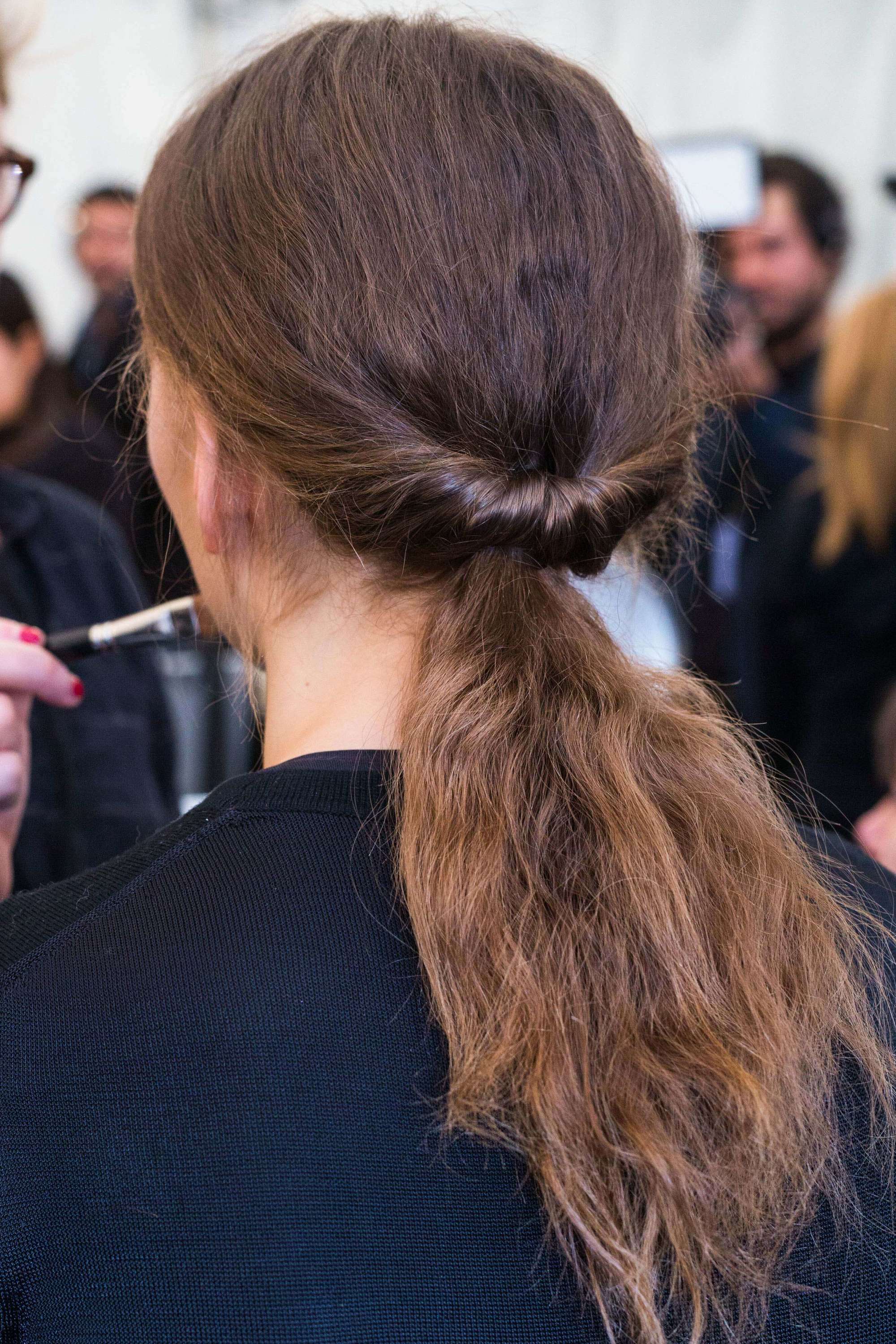 Back view of woman with medium length brown naturally wavy hair styled in a ponytail tuck in backstage runway picture