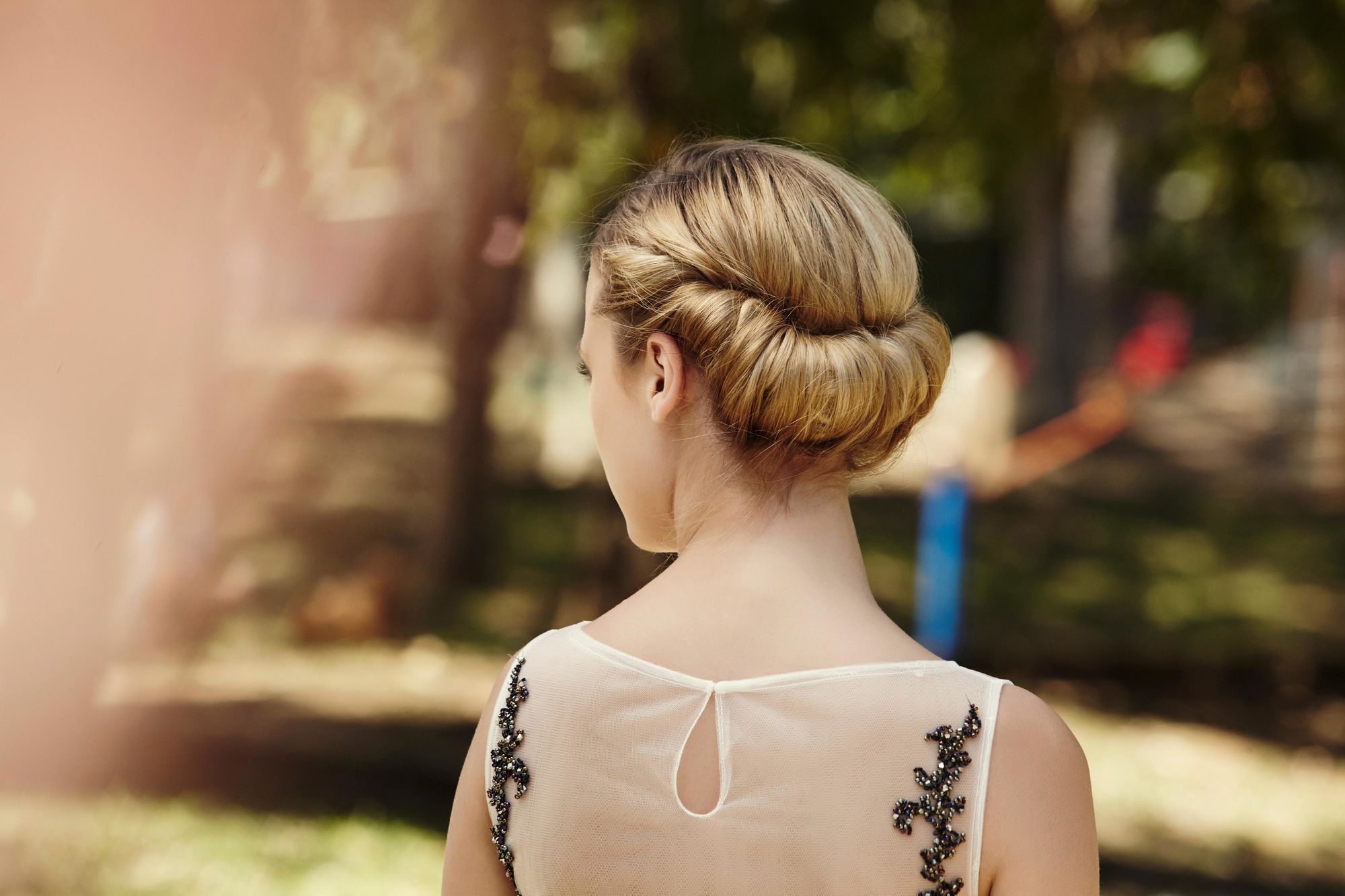 updos for long hair: blonde model with long hair styled into a rolled chignon wearing a black dress with sheer back