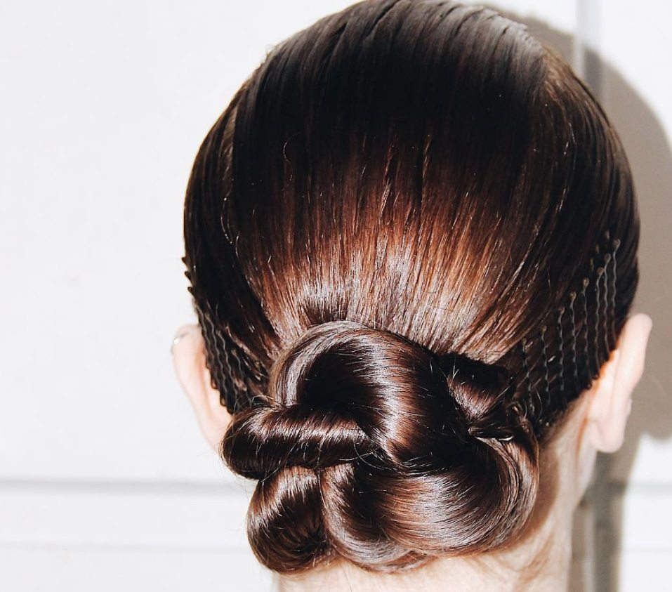 Updos for long hair: Woman with brown hair in sleek low twisted nun with stacked bobby pins along the side.