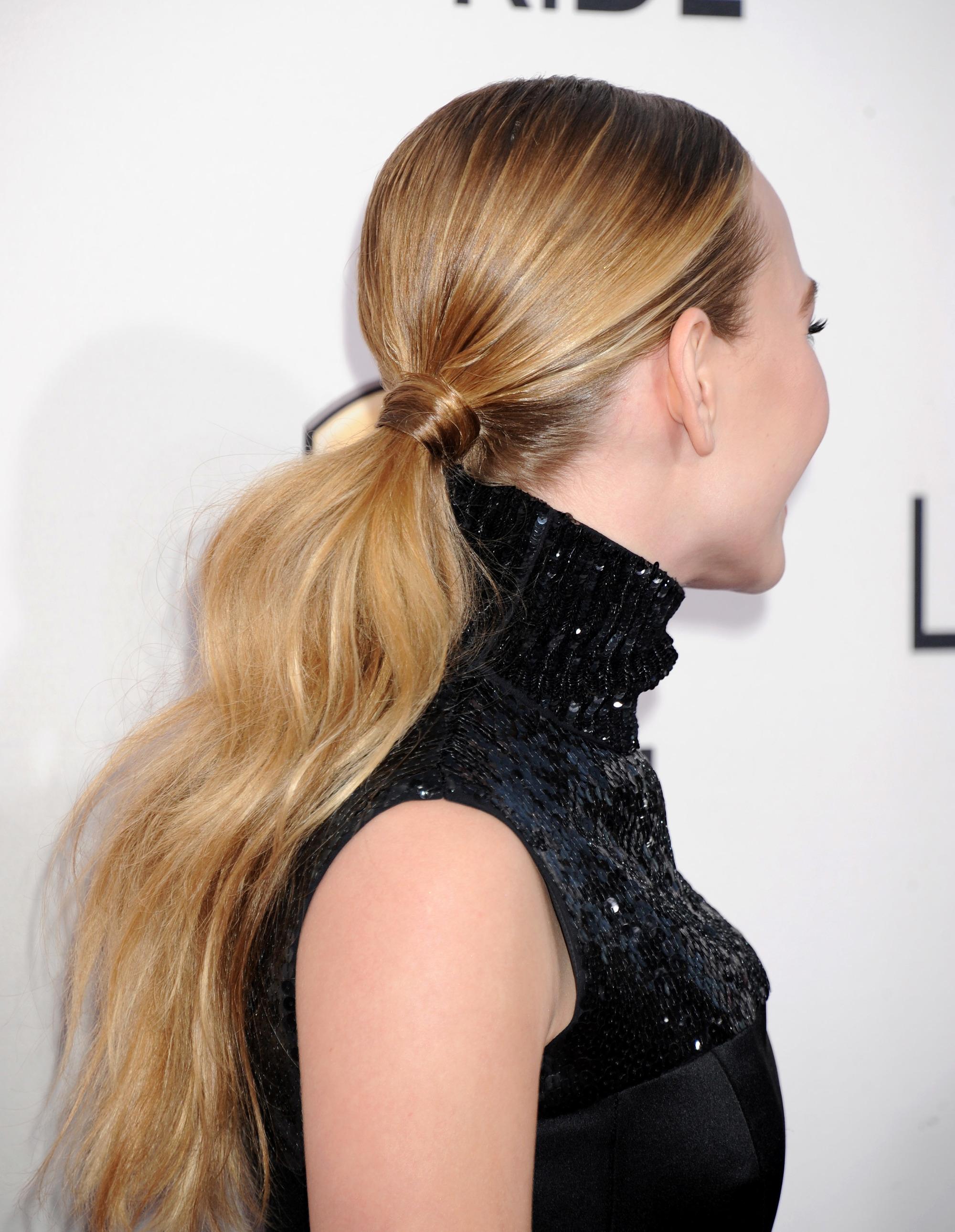 Ponytail ideas: Side shot of Britt Robertson with long dark blonde hair styled into a low, wavy ponytail, wearing a black sequin top and posing on the red carpet