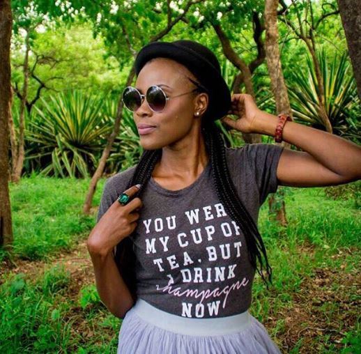 woman with box braids wearing a slogan t-shirt, sunglasses and a hat in the trees