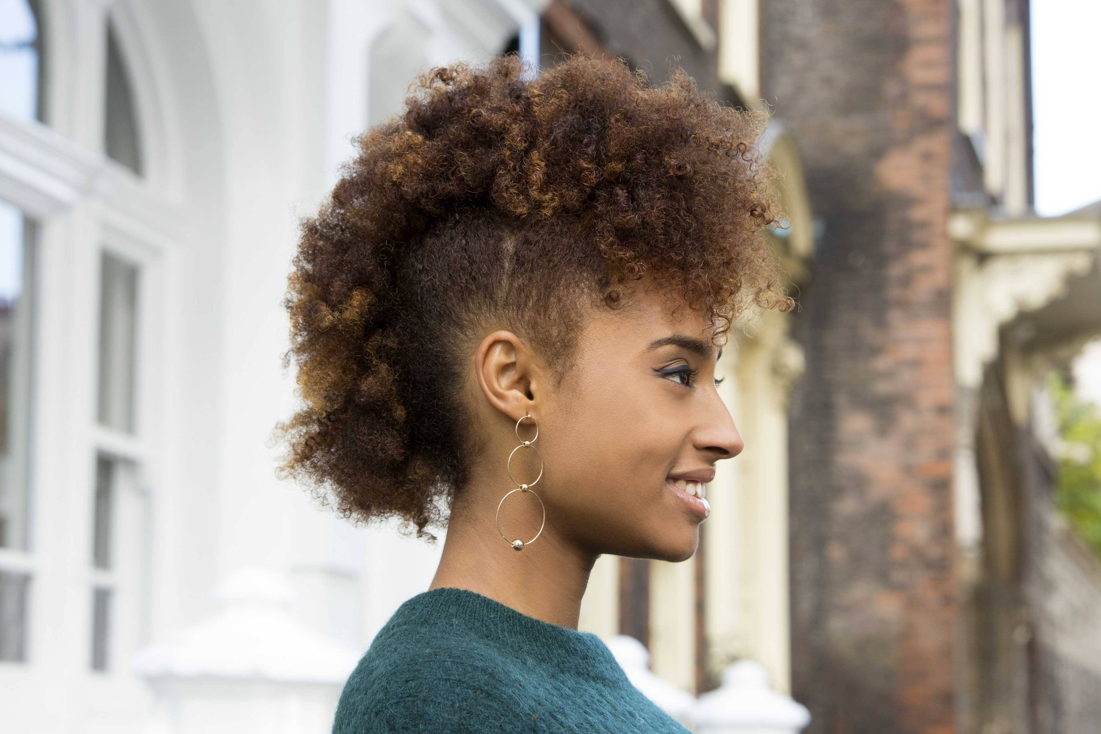 Christmas hairstyles: Woman with naturally curly hair in frohawk wearing a green jumper.
