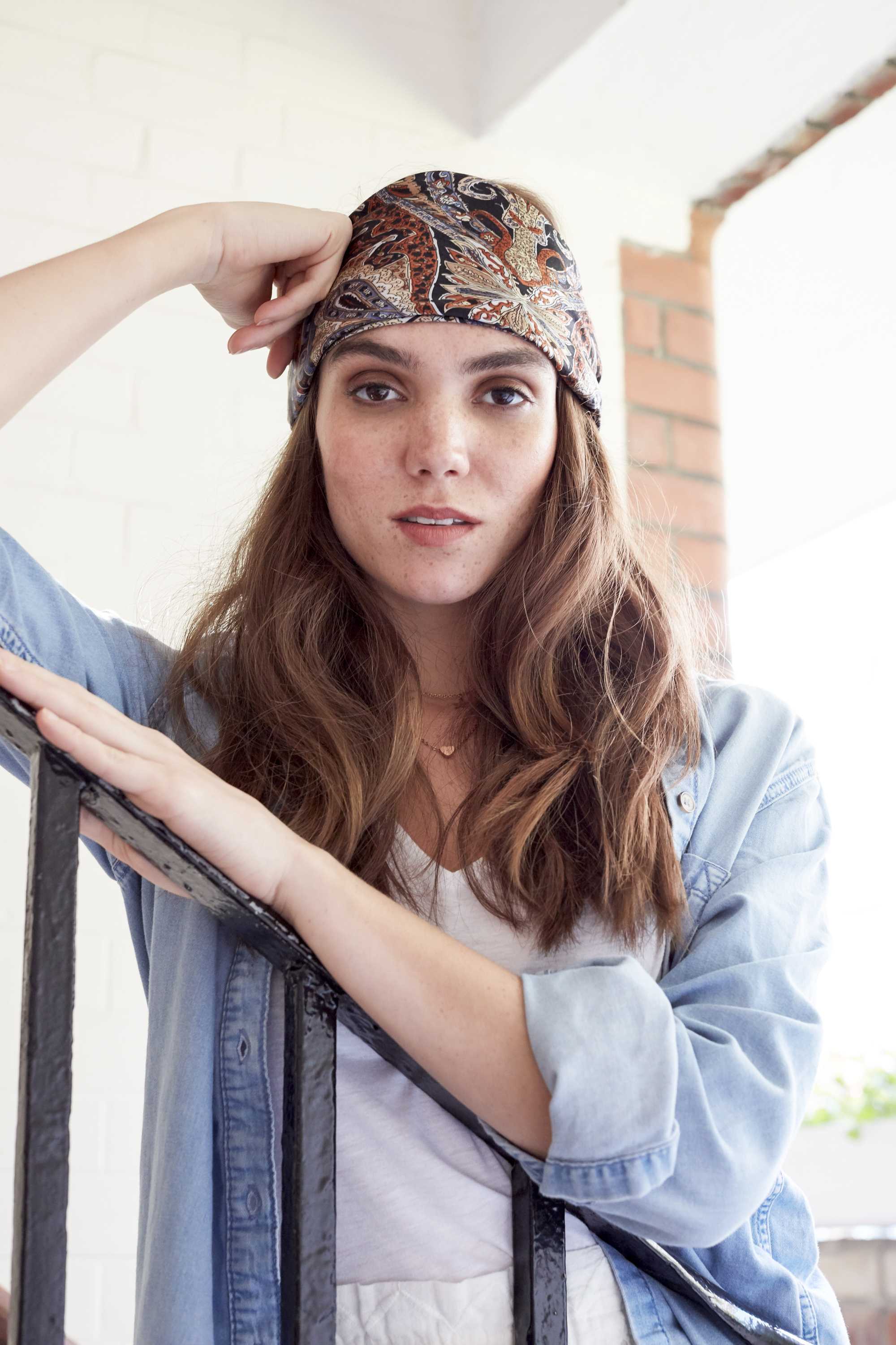 freckled brunette model with long curly hair with a paisley patterned scarf tied around her head, wearing a denim shirt and standing on a stairwell