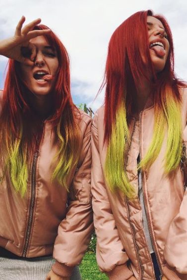 Bella with twin sister Dani Thorne posing wearing pink jackets and long straight hair dyed in a red to yellow ombre