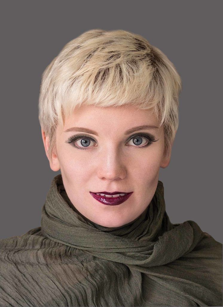 close up shot of a woman wearing a khaki green outfit with her blonde hair cut into a pixie crop with a textured fringe