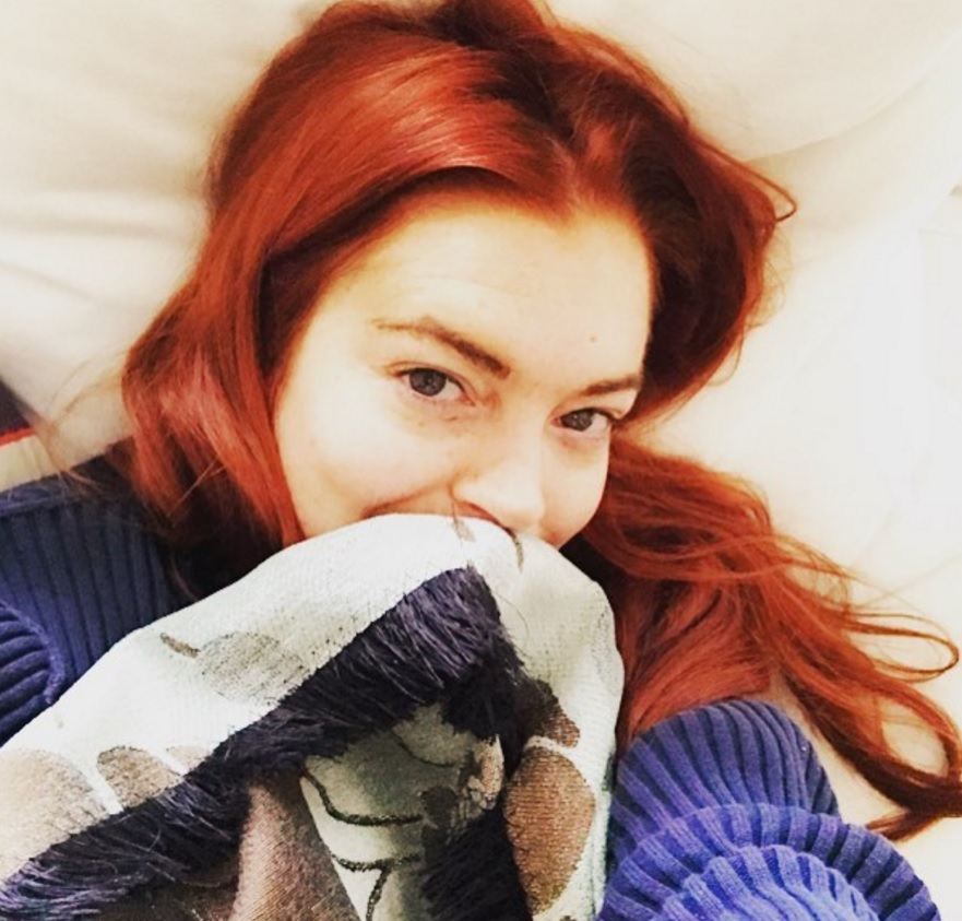 Lindsay Lohan selfie with vibrant read hair wearing a blue and white sweater