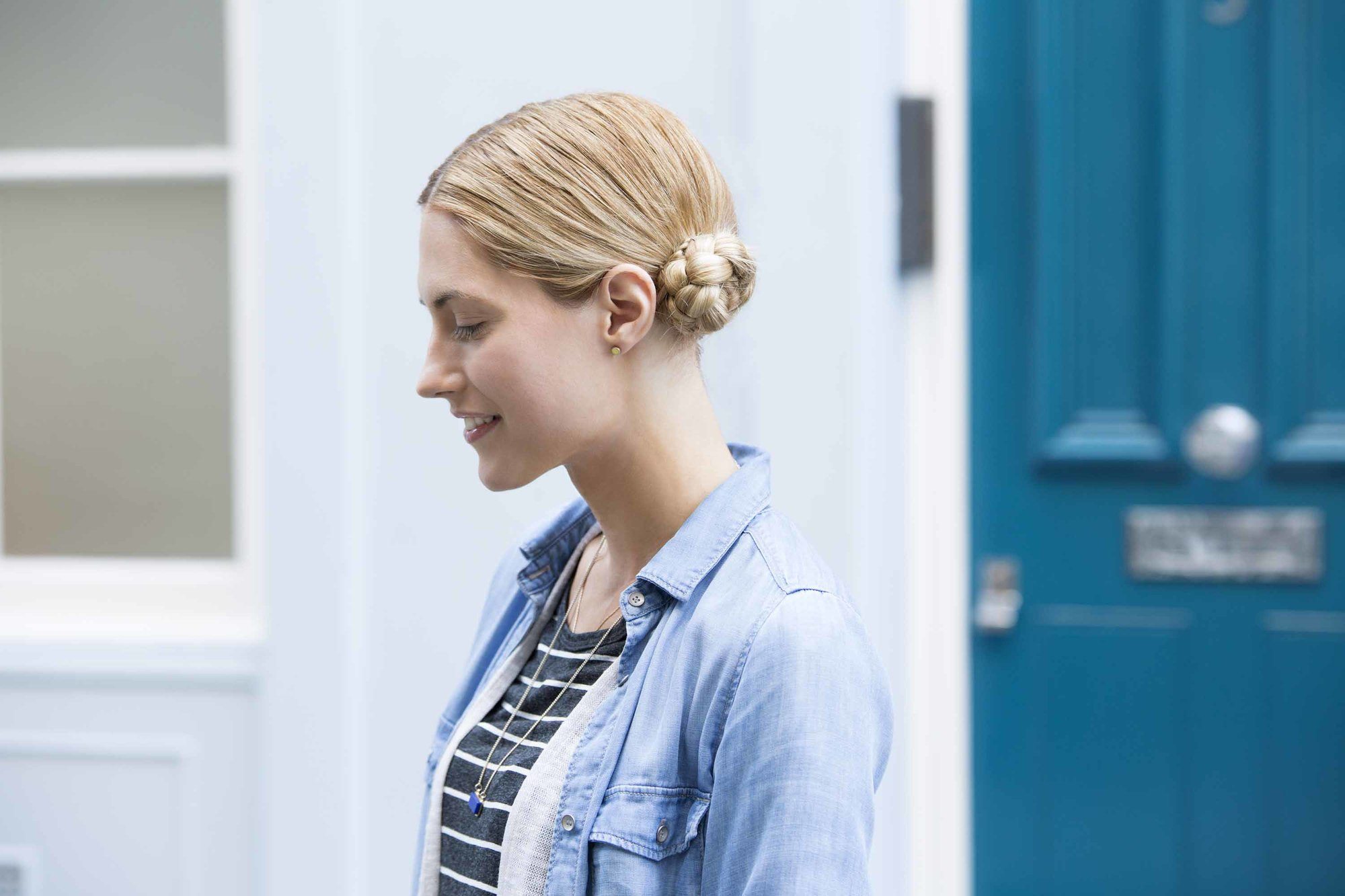 Updos for long hair: Model with blonde braided low space buns outside wearing a striped tshirt and denim shirt jacket