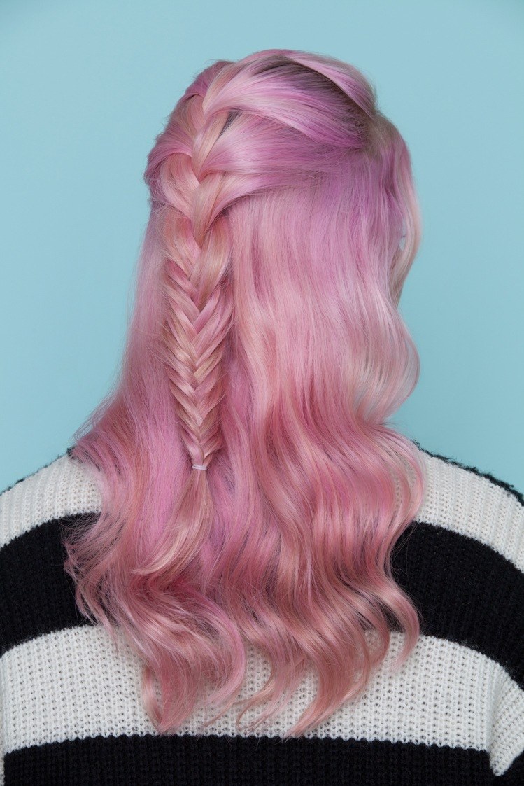 the back view of a young woman with pink coloured hair wearing a French fishtail braid half updo