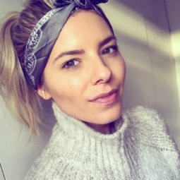 Mollie King wearing a printed bandana in her blonde hair styled into a high ponytail wearing a light grey sweater