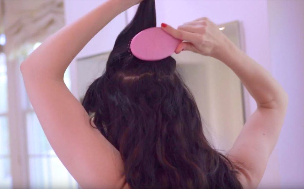 a rear view of a woman combing up her wavy long brunette hair