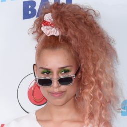 Curly hair hairstyles: Singer Raye with light pink naturally curly hair in high scrunchie ponytail on red carpet wearing sunglasses