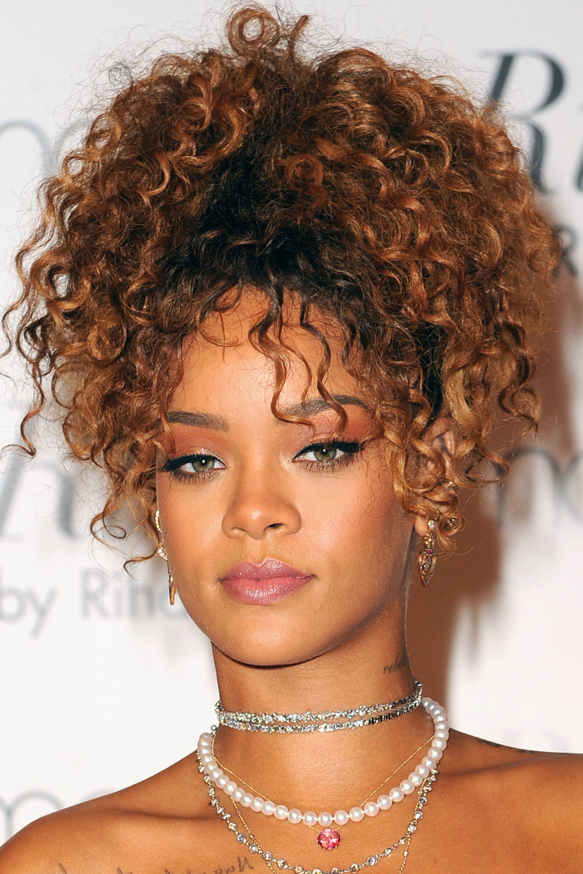 Curly hair hairstyles: Rihanna with golden brown curly hair in high pineapple ponytail updo on red carpet wearing a pearl necklace