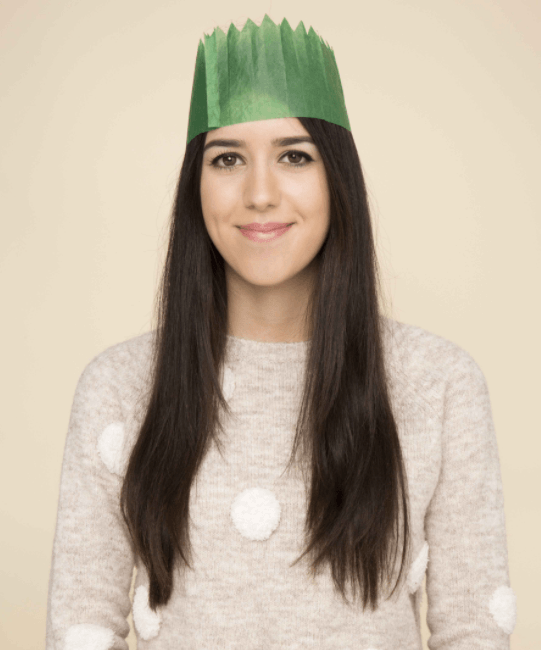 Christmas hairstyles: Brunette woman with long straight brown hair wearing a green party hat and spotted knitted jumper.
