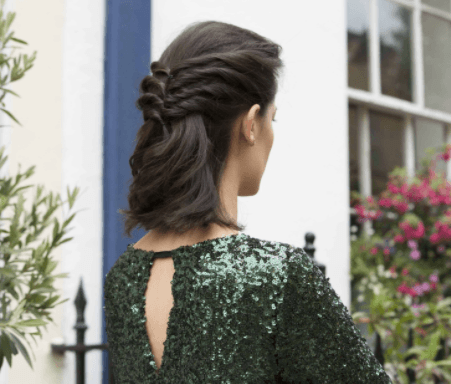 Christmas hairstyles: Woman with wavy brown hair in half-up twisted style wearing a green glitter dress.