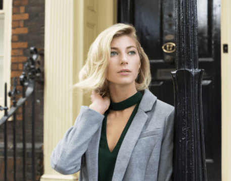 Christmas hairstyles: Blonde woman with hair styled in a flipped out bob wearing a grey blazer over a black top touching her hair.