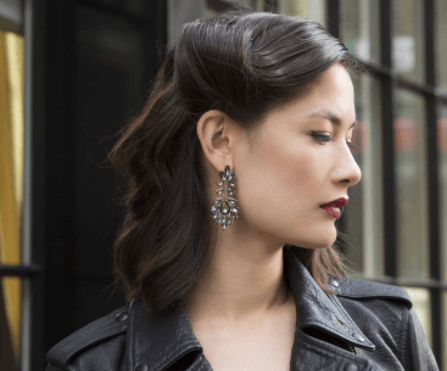 Christmas hairstyles: Woman with dark brown hair in vintage retro glam roll wearing a black leather jacket and jewelled earrings.