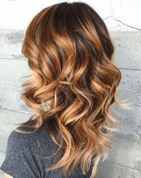 side view of a woman with shoulder length curled hair with caramel and brown tones