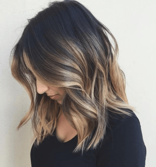 side view image of a woman with her shoulder length hair worn down and wavy with dark roots