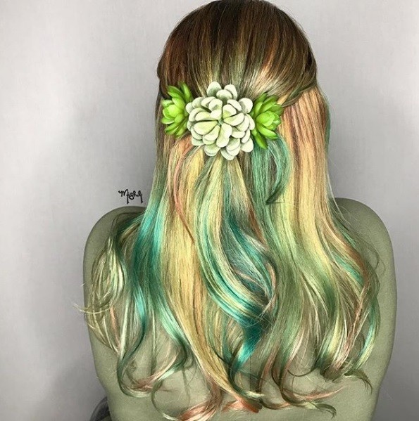 back view of a woman with long wavy green and golden blonde hair styled in a half up half down with succulent hair accessories