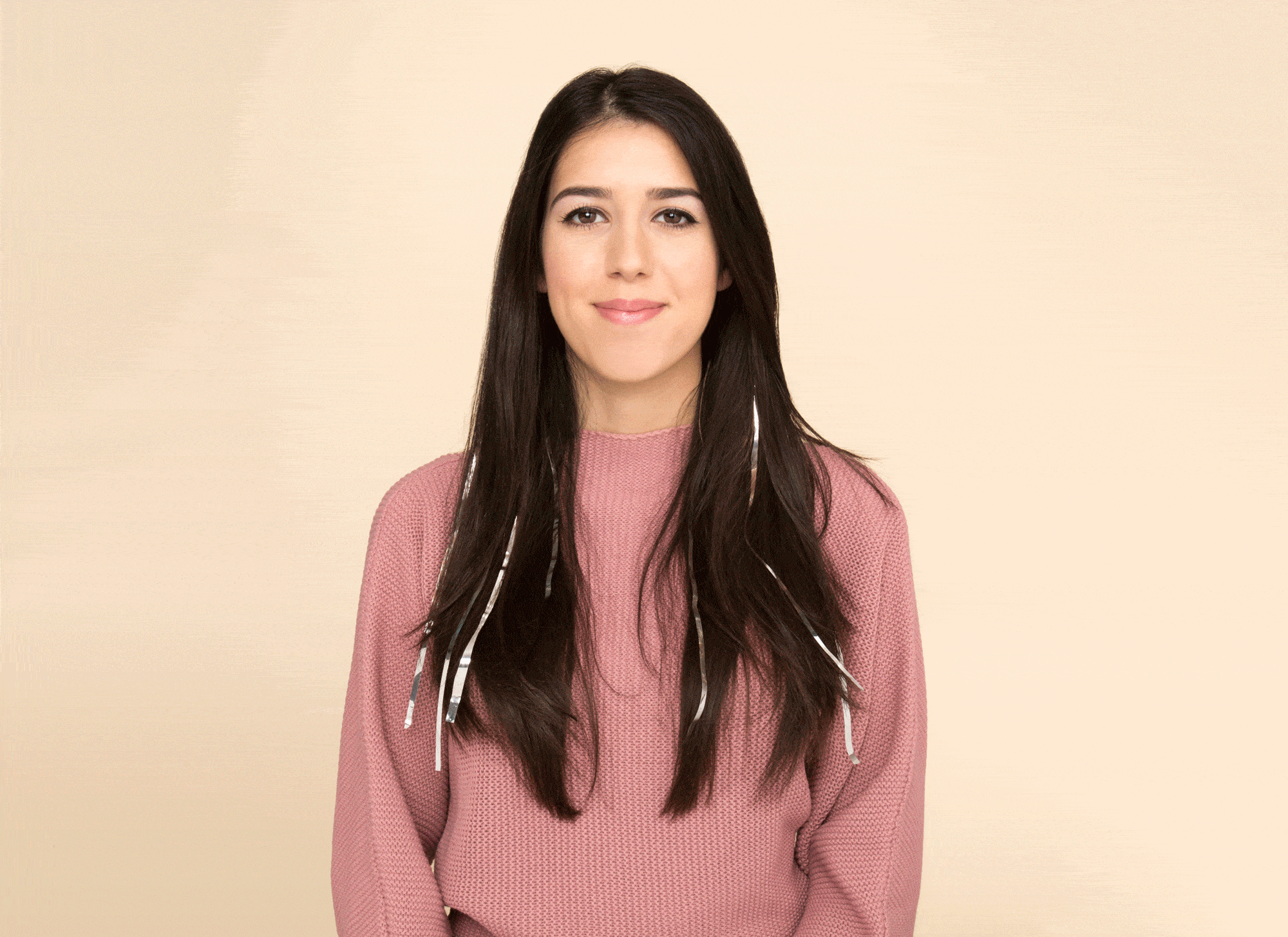 Christmas hairstyles: Woman with long dark brown hair with strips of tinsel wearing a pink jumper.