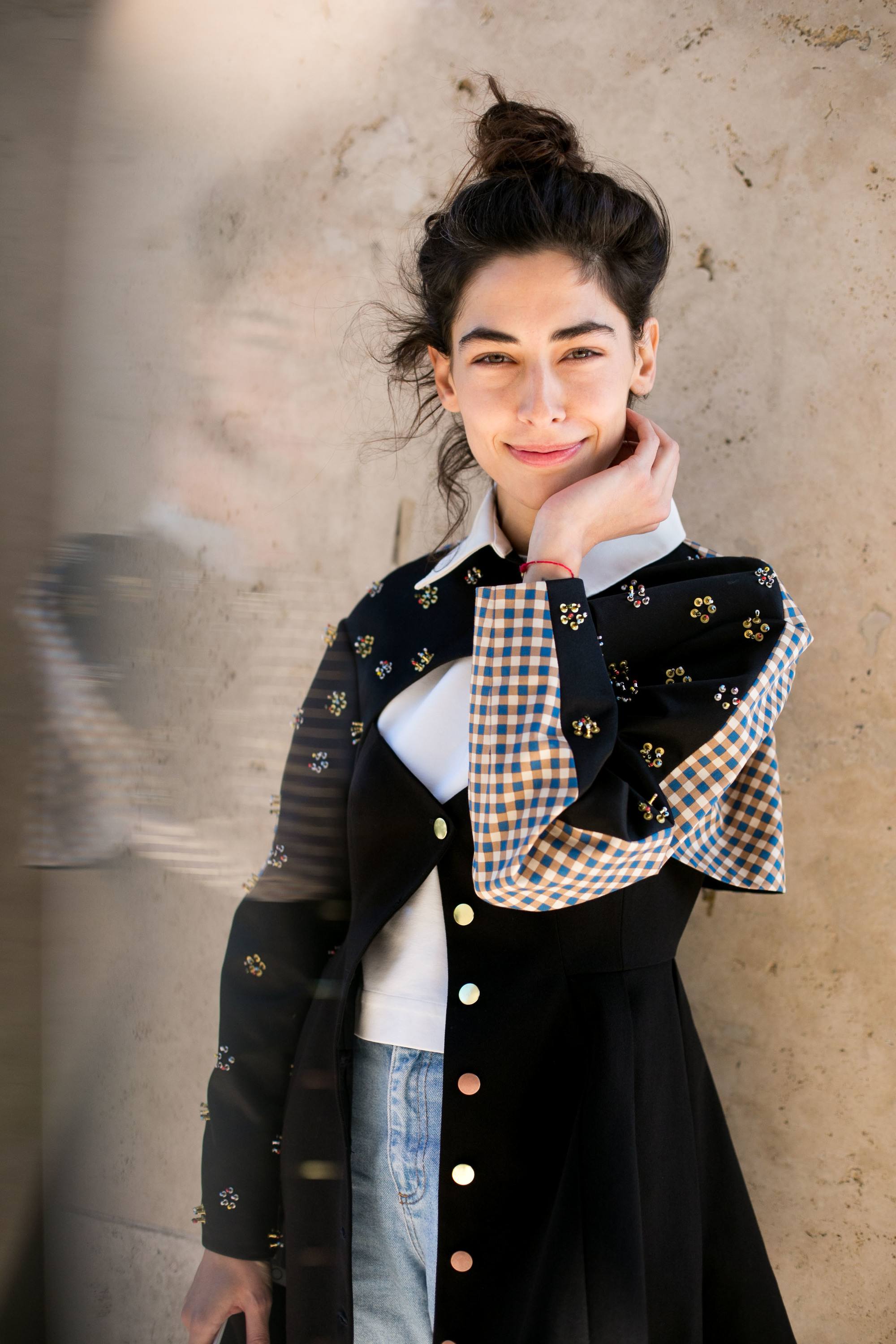 natural wavy hair: close up shot of dark haired street style model with wavy topknot, wearing black jacket and denim dress, and posing on the street