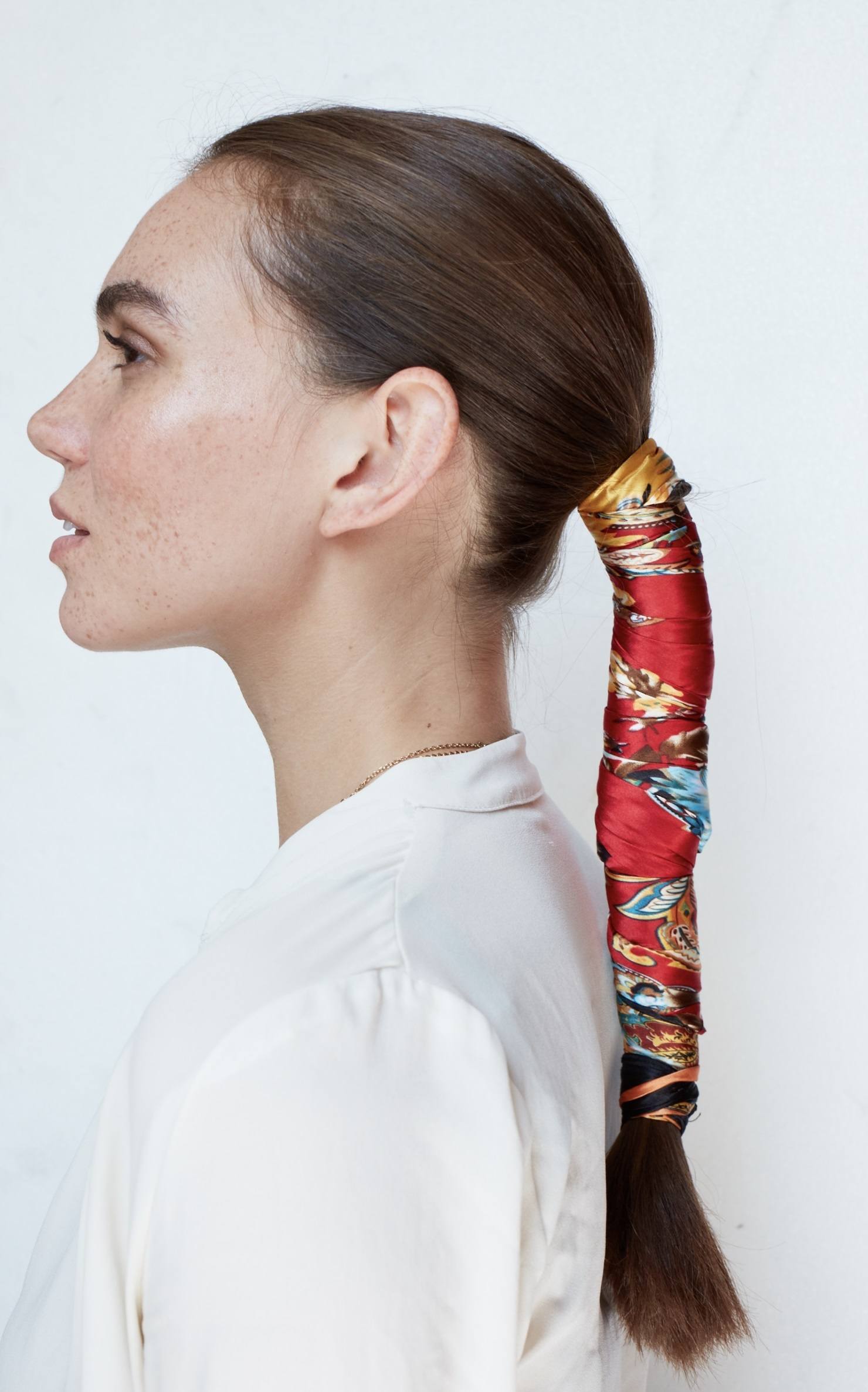 side profile shot of a brunette model with her hair in a low ponytail wrapped in a colourful red silk scarf