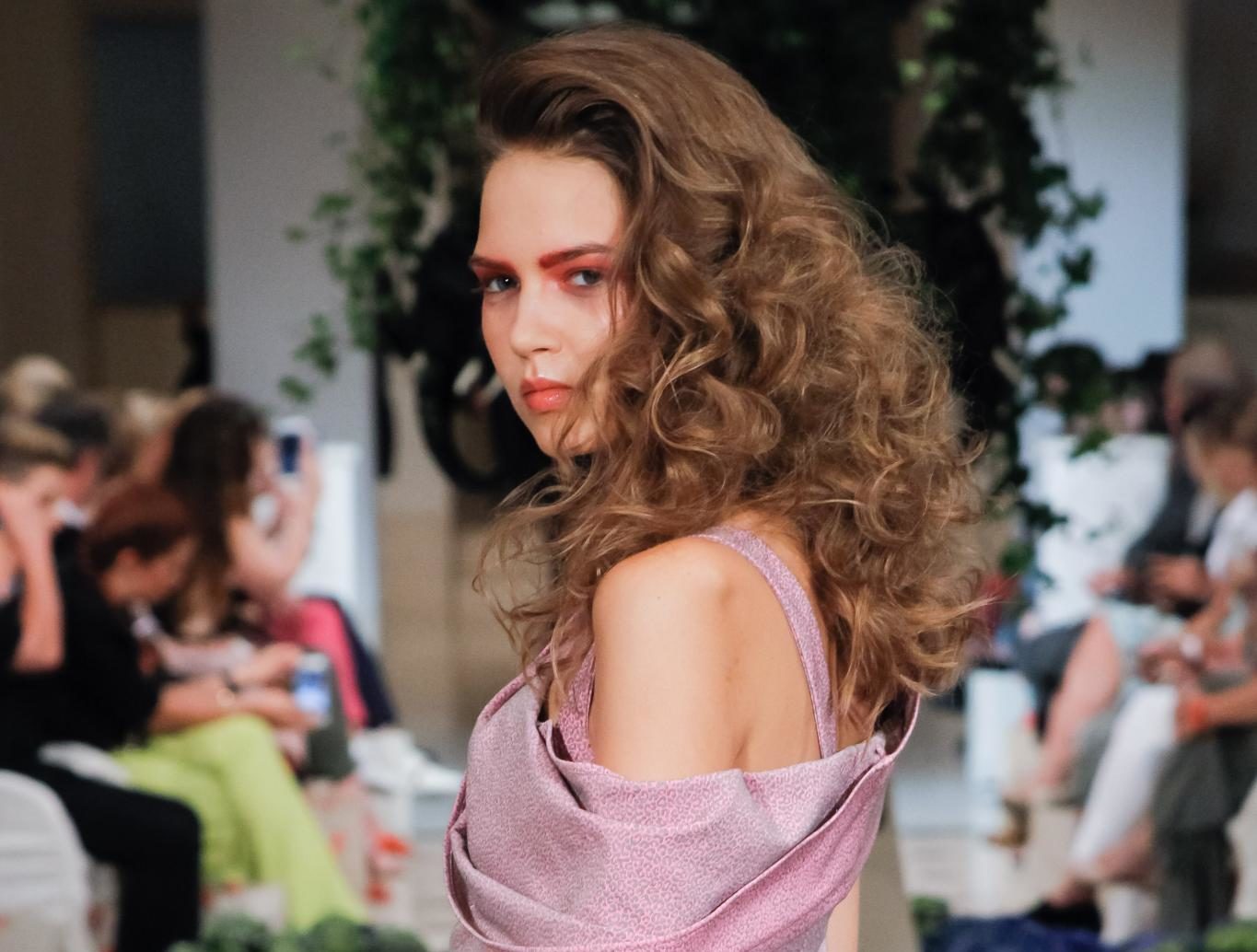 Retro hairstyles: Close up shot of a woman with light brown medium hair styled into a big, voluminous waves walking on the Anja Gockel runway