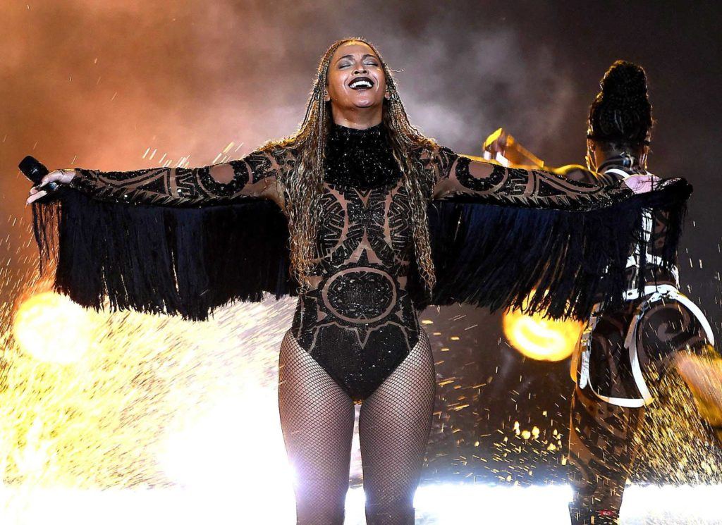close up shot of beyonce on the stage with box braids, wearing black bodysuit and preforming