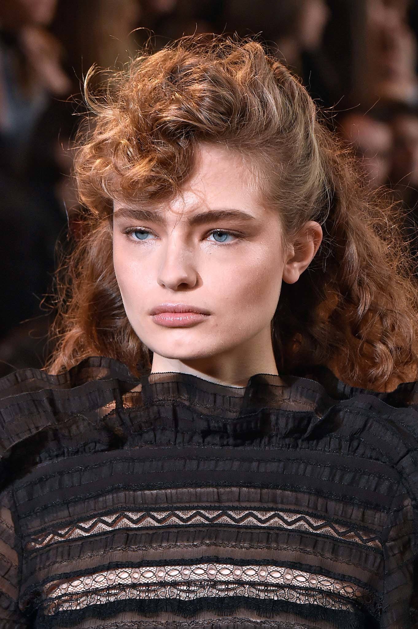 Retro hairstyles: Close up shot of a woman with light brown naturally curly hair styled into fauxhawk walking on the Isabel Marant runway