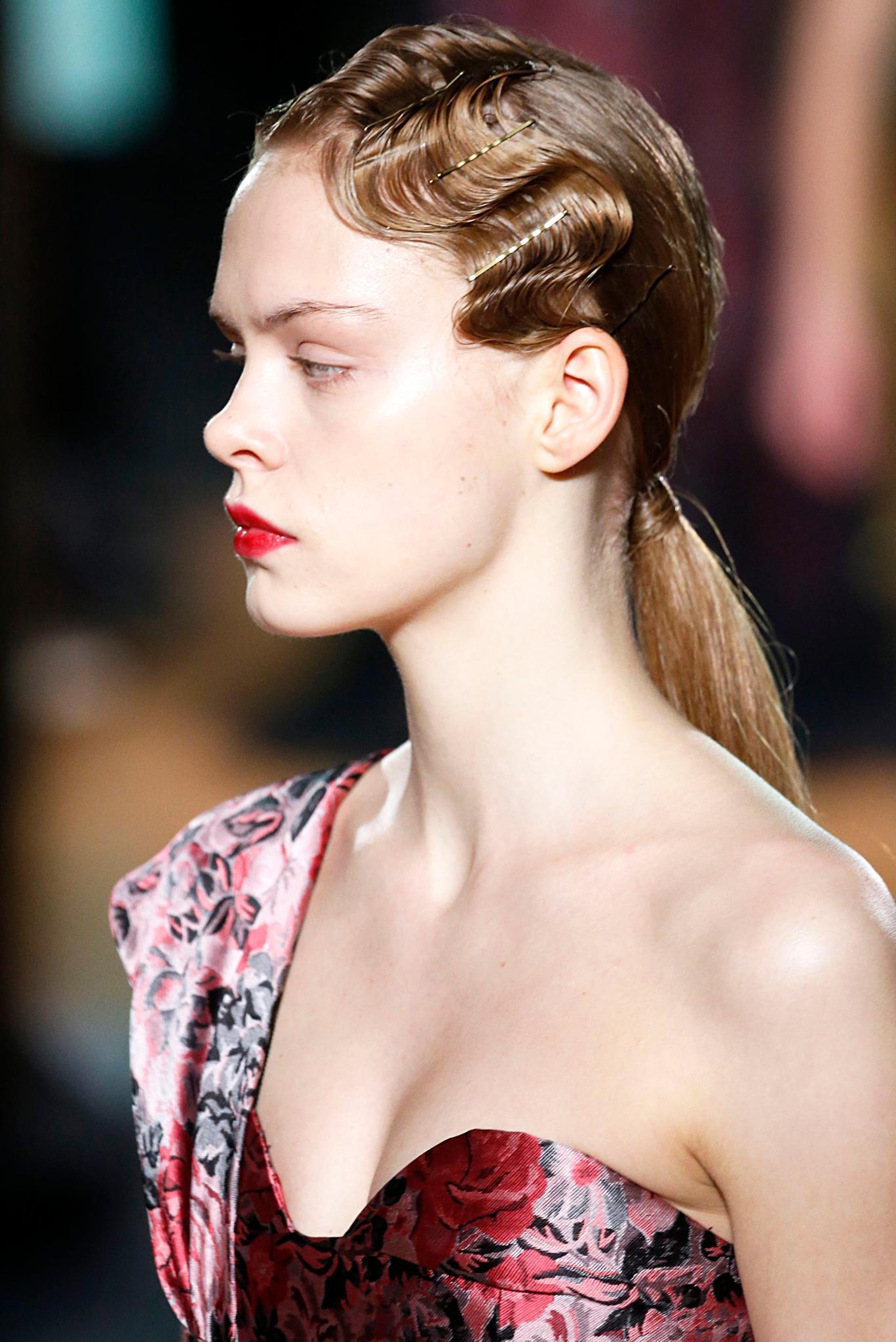 Retro hairstyles: Close up side shot of a model with dark blonde hair styled into a low ponytail with finger waves detailing. complete with bobby pins, wearing pink on Erdem runway