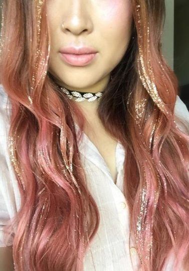 close up photo of a woman with long pink curly hair with gold glitter glitterage balayage