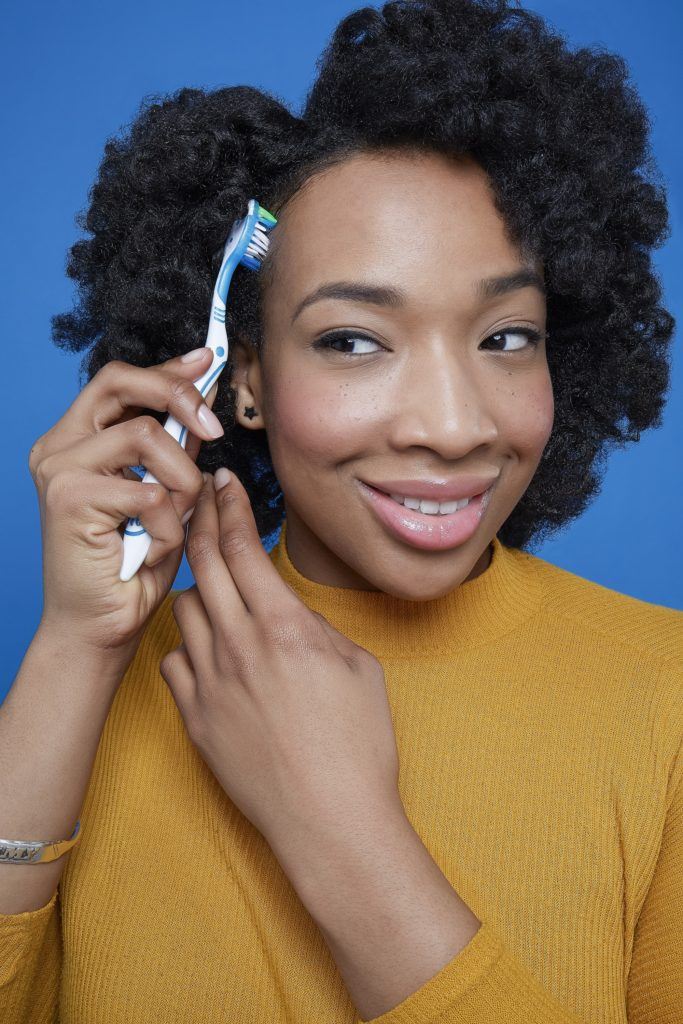 Black woman holding toothbrush to hair laying edges with flexi rod curls