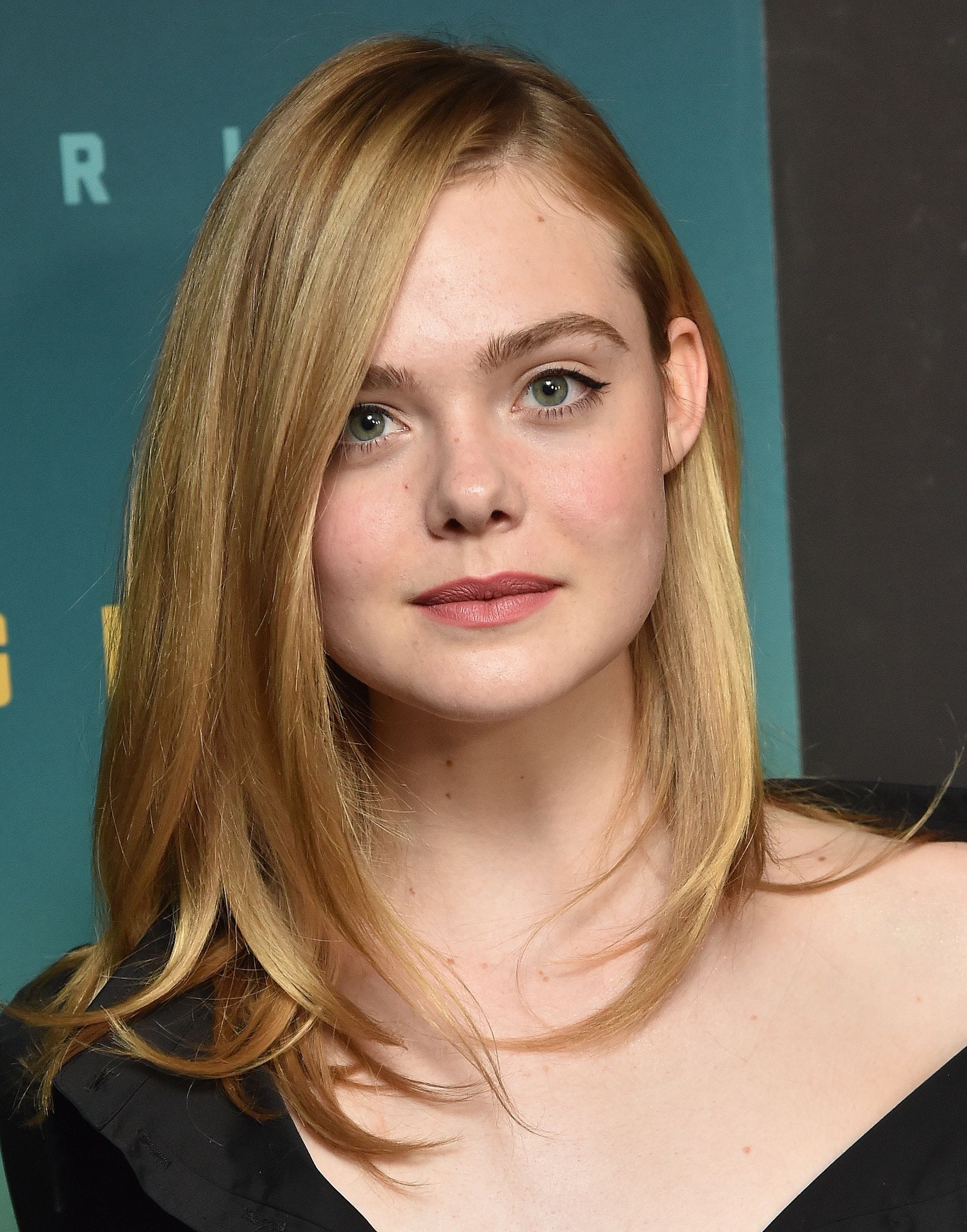 Red carpet hairstyles: Elle Fanning with straight blonde shoulder length hair parted down the side wearing a black dress.