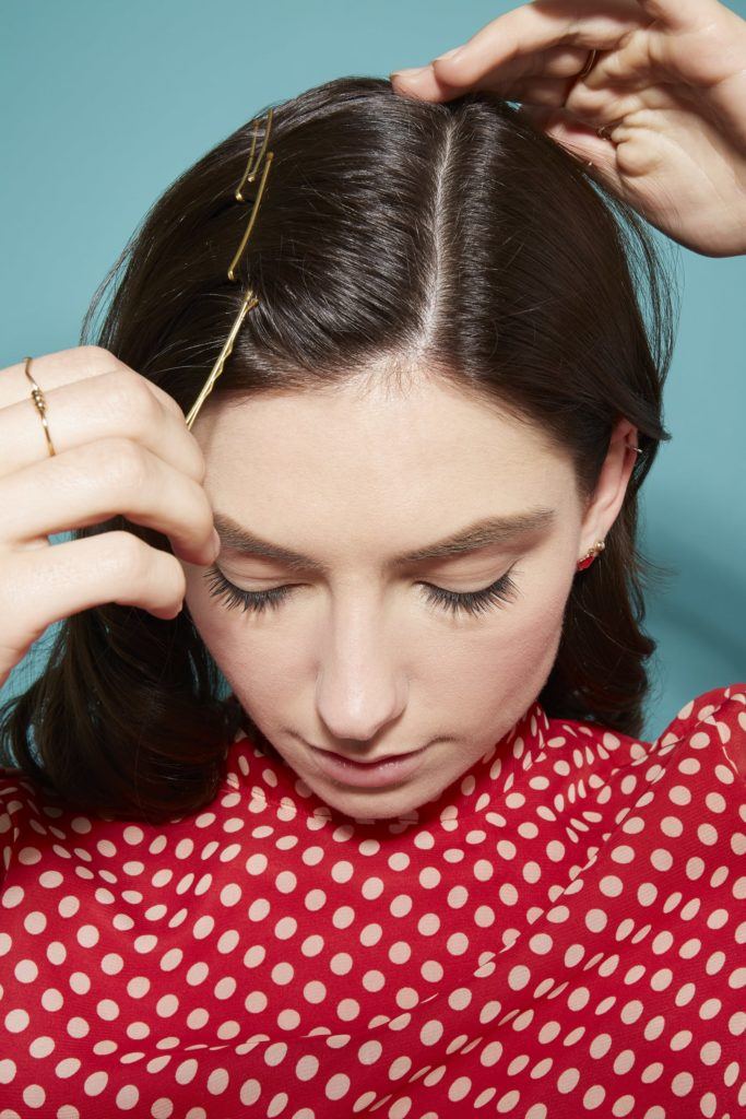 woman with dark brown glossy hair in loose curls pinning her hair in place and wearing a red and white spotted dress
