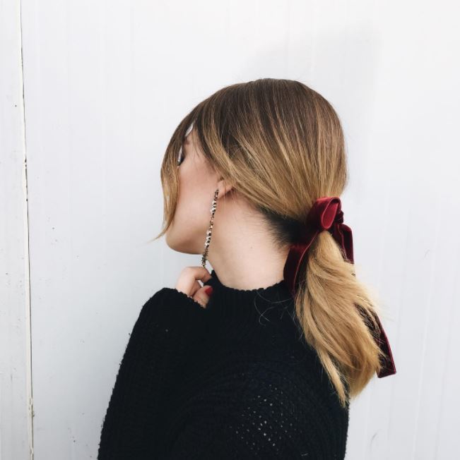 side view of dirty blonde hair in low ponytail with deep red velvet ribbon around base of ponytail