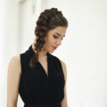 brunette model with a thick side braided ponytail wearing a black v neck dress