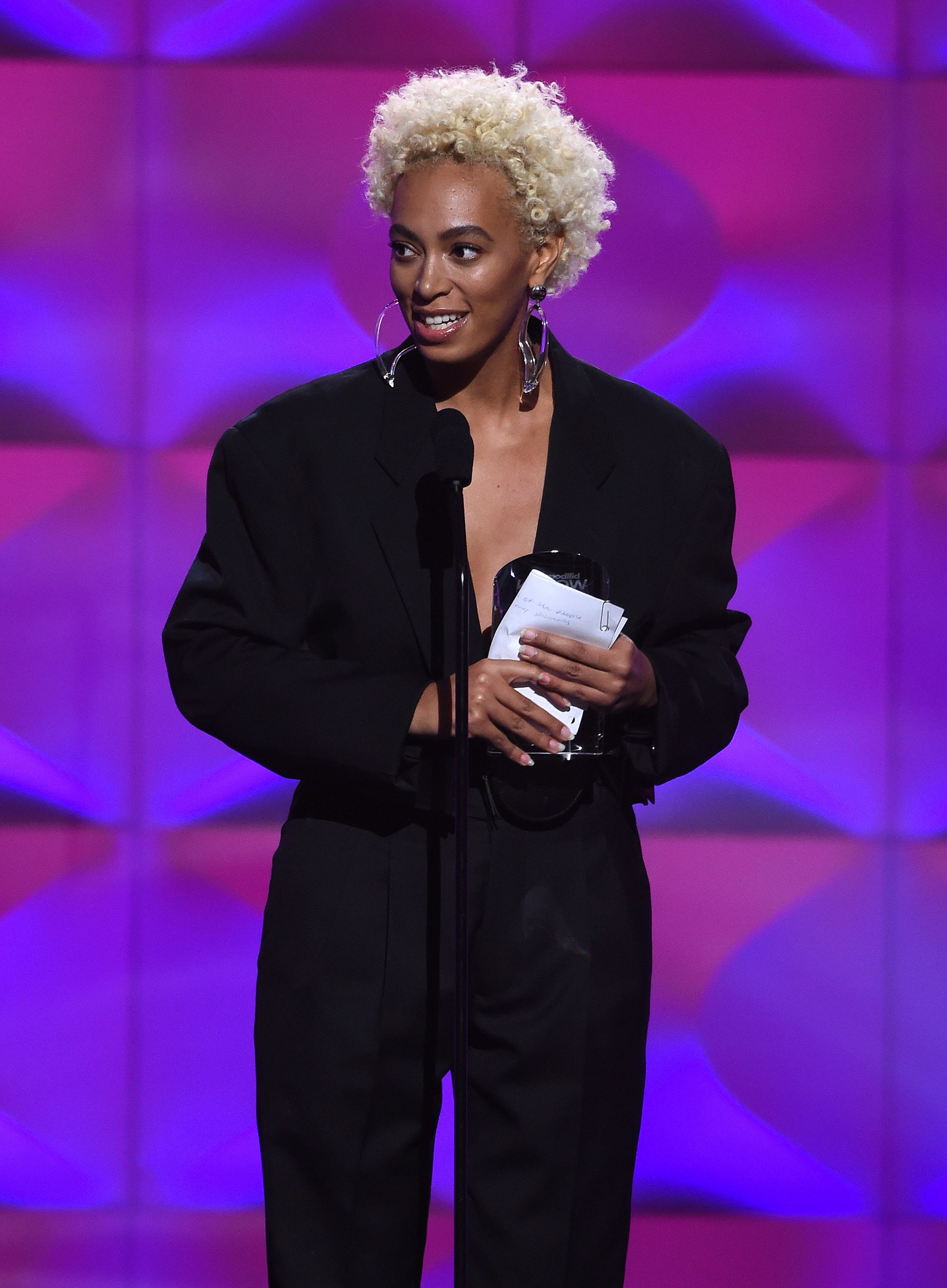 close up shot of solange knowles with blonde afro hairstyle, wearing black jumpsuit and accepting award at the billboard women in music awards